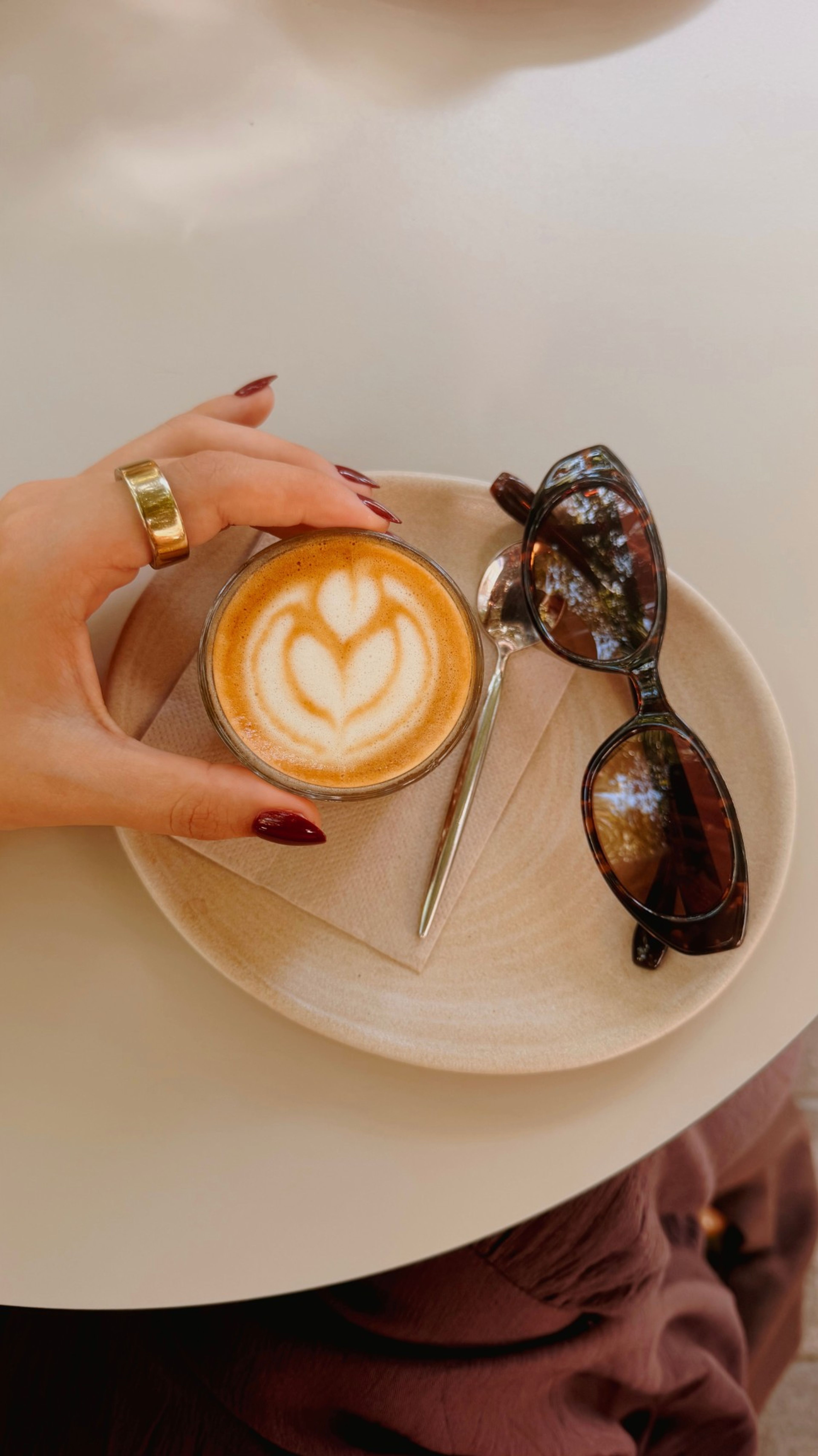 Hand holding a coffee with latte art next to sunglasses