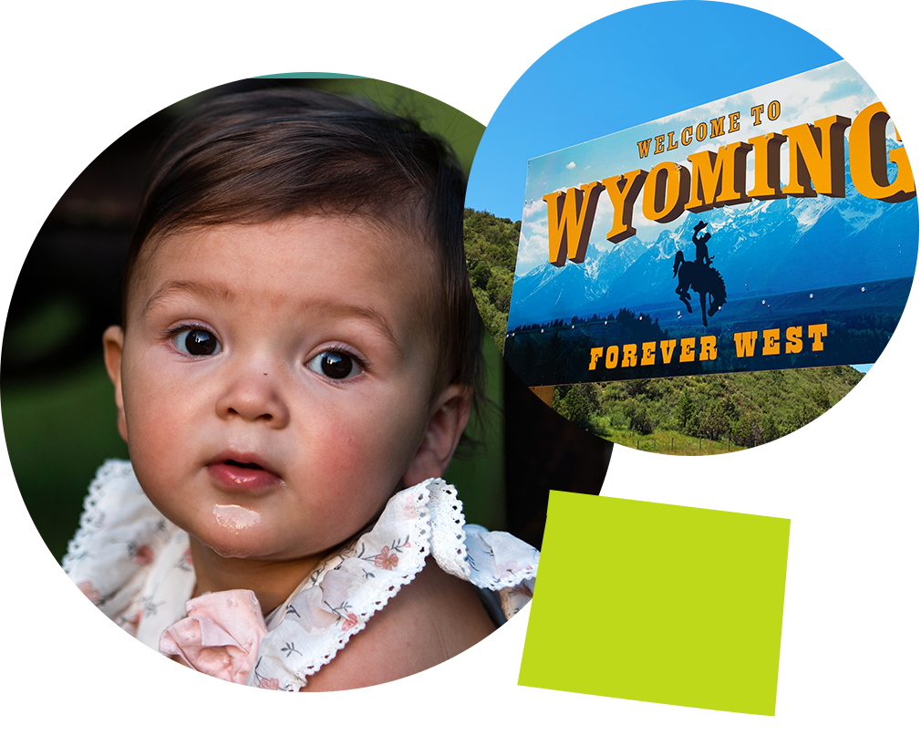 Baby girl in a white dress next to a sign that reads Welcome to Wyoming, Forever West