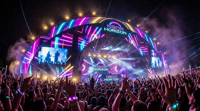 A vibrant scene from a music festival showing a stage with curved LED screens displaying visuals and performers, creating an immersive nighttime experience.