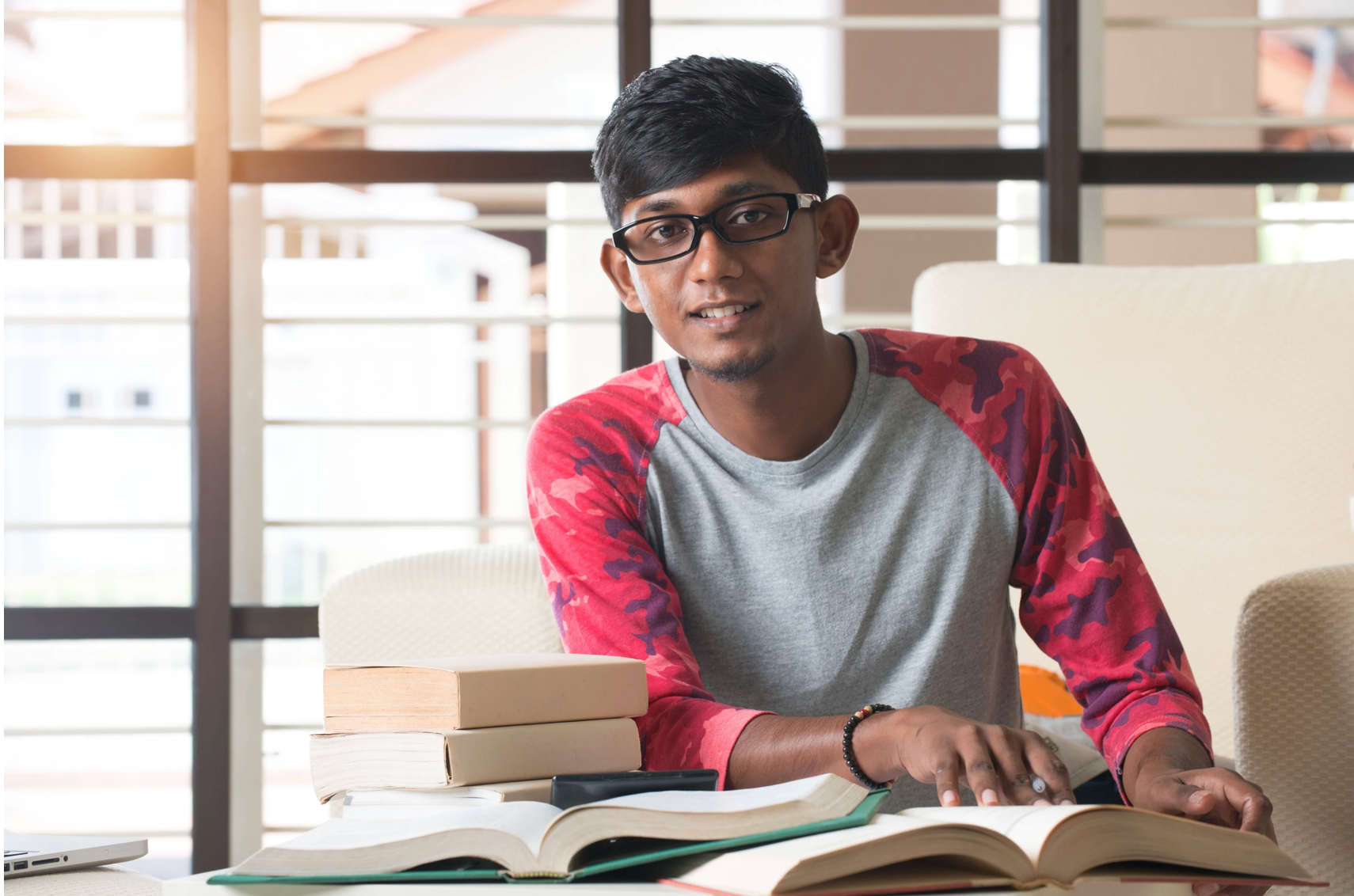 Student studying with open books at a desk, preparing for exams in a bright study environment, representing focused learning and academic success.