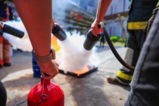 Firefighters conducting a live fire training exercise, using handheld extinguishers and a hose to suppress a controlled blaze on a training pad.