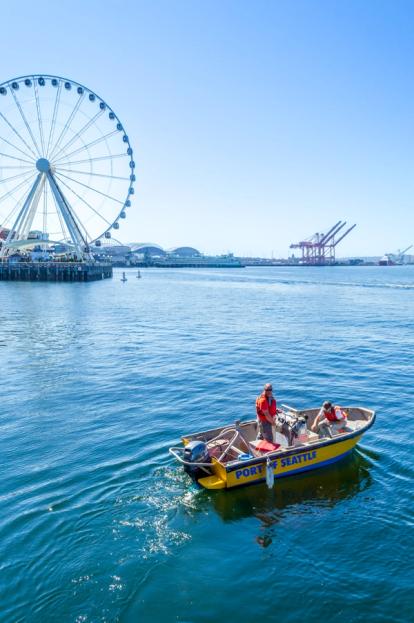 Two people on small boat deploying equipment with a ferris wheel in the background