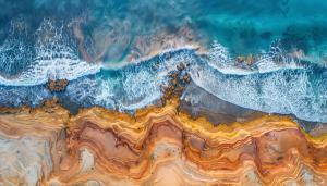 Ariel view of rocky coastline with colourful sand beside ocean with waves 