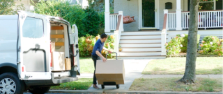 Male Courier Using Trolley To Deliver Package From Van To House