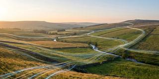 Abstract digital data lines flowing through a tranquil rural landscape at sunrise, symbolizing global network connectivity and modern information technology.