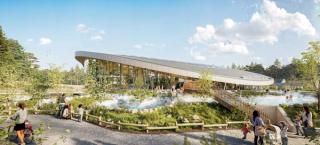 A contemporary wellness and recreation facility with a sweeping curved roof and floor-to-ceiling glass walls sits within a lush landscaped setting. Outdoor heated pools and winding water features are surrounded by native vegetation, rocks, and wooden pathways. Visitors relax, swim, stroll, and gather throughout the space, while trees and forested areas frame the site under a bright blue sky with scattered clouds.