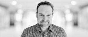 Headshot of Tim Greenhill with a blurred office background behind him