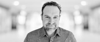 Headshot of Tim Greenhill with a blurred office background behind him