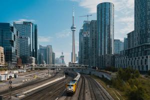Freight train travelling through downtown Toronto near the CN Tower, with high-rise residential buildings along the rail corridor.