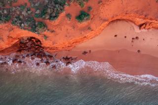 Ariel view of rocky coastline with colourful sand beside ocean with waves 