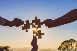 three hands holding puzzle pieces coming together in an alliance