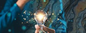 Person holding a sparkling light bulb with rock textures in the background