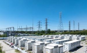 White energy storage units with transmission power lines in the background, against a blue sky