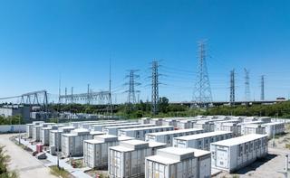 White energy storage units with transmission power lines in the background, against a blue sky