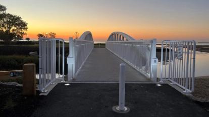 An evening view of the pedestrian bridge showing the safety fencing, bollards, and recessed lighting on the bridge.