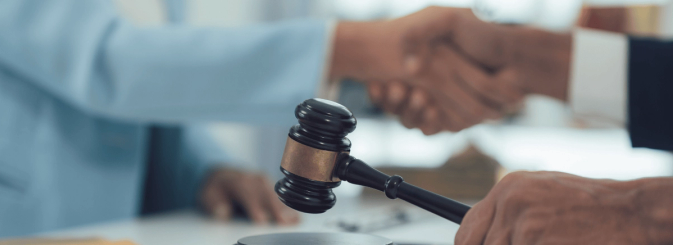 A man and a woman shaking hands alongside a gavel striking