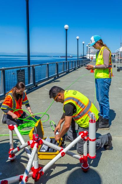 Three people in high vis vests preparing equipment on a pier