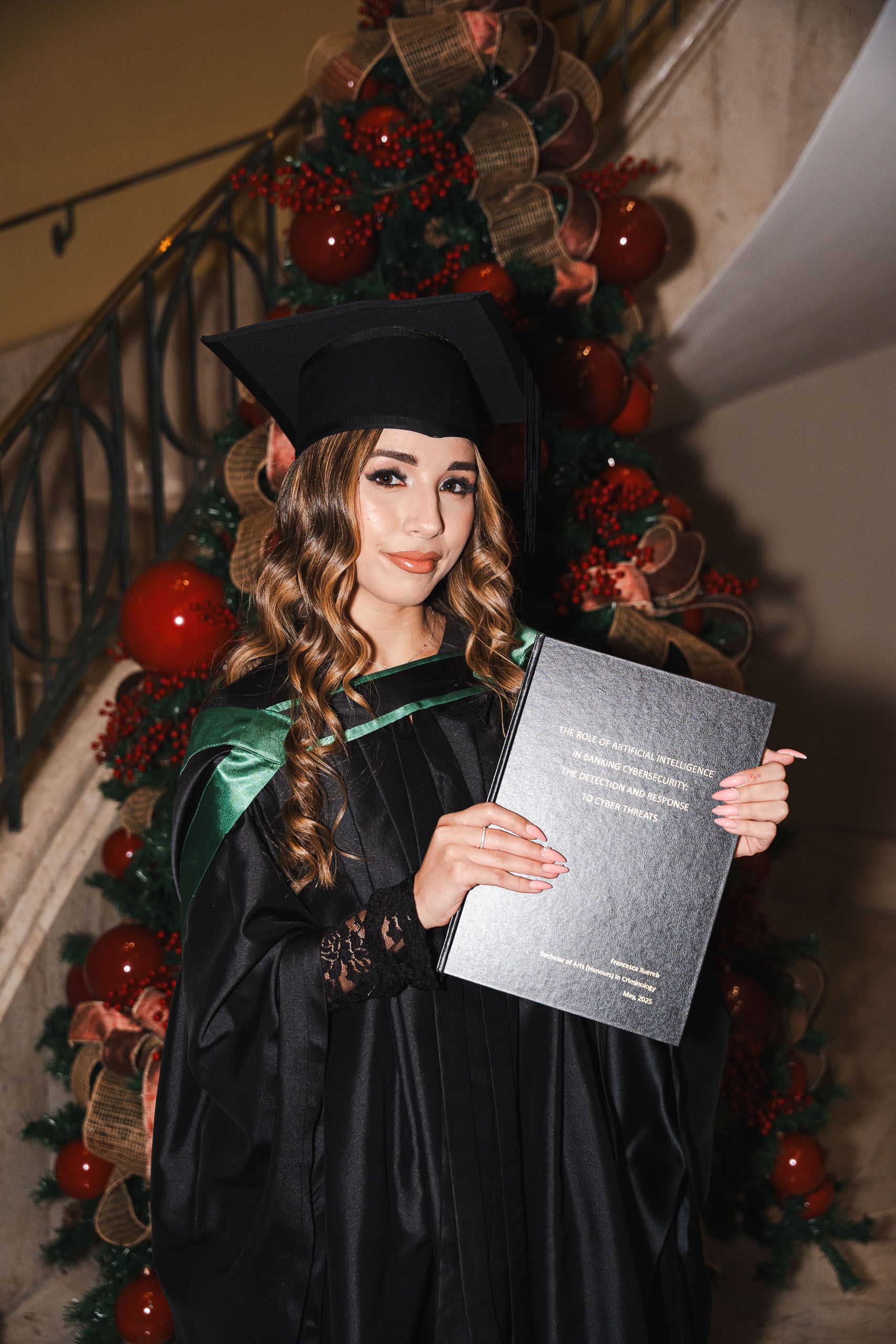 Graduate holding her thesis beside a Christmas tree at Corinthia Palace Malta
