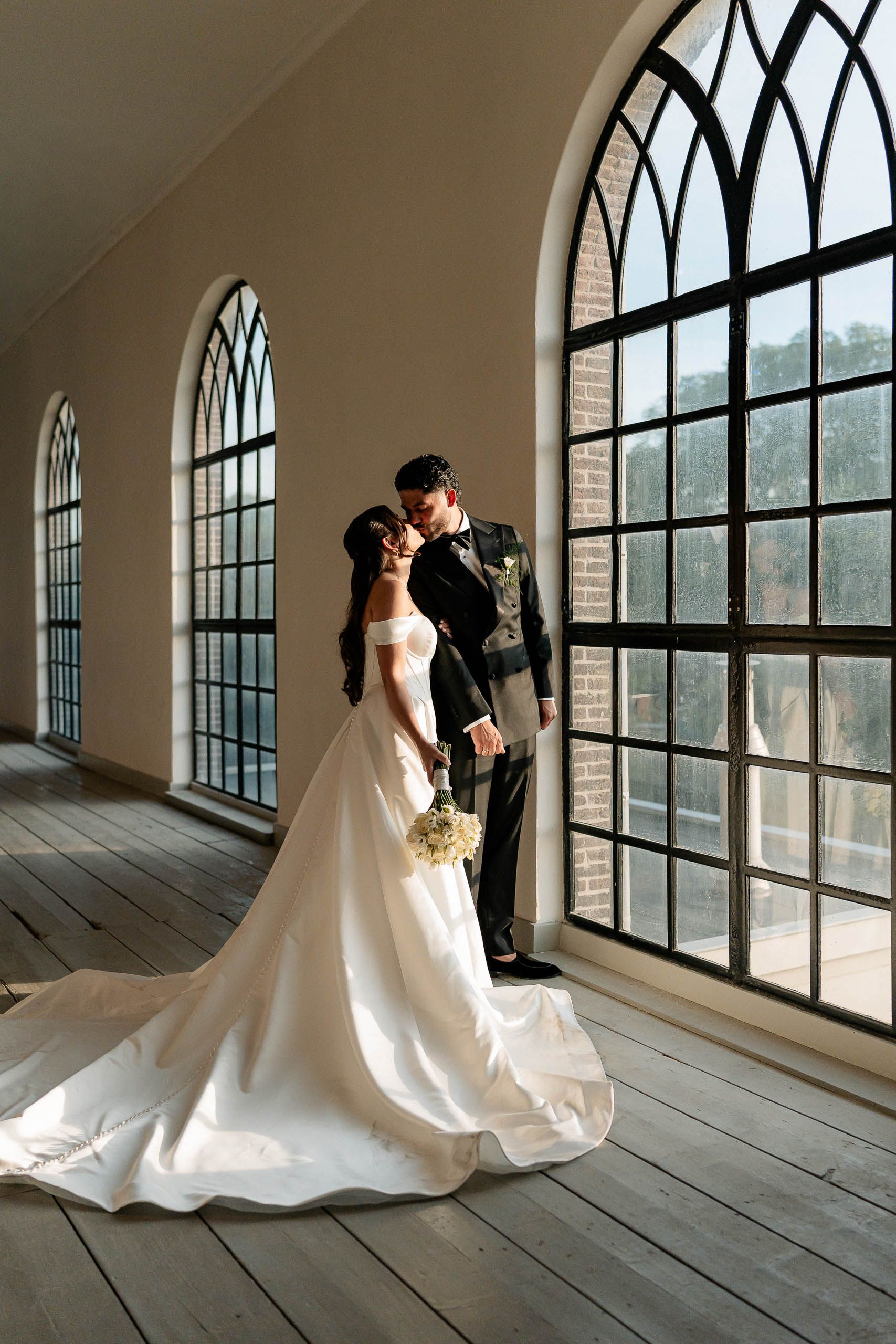 Bride and groom kissing beside arched windows during their church wedding in Den Helder, Netherlands.