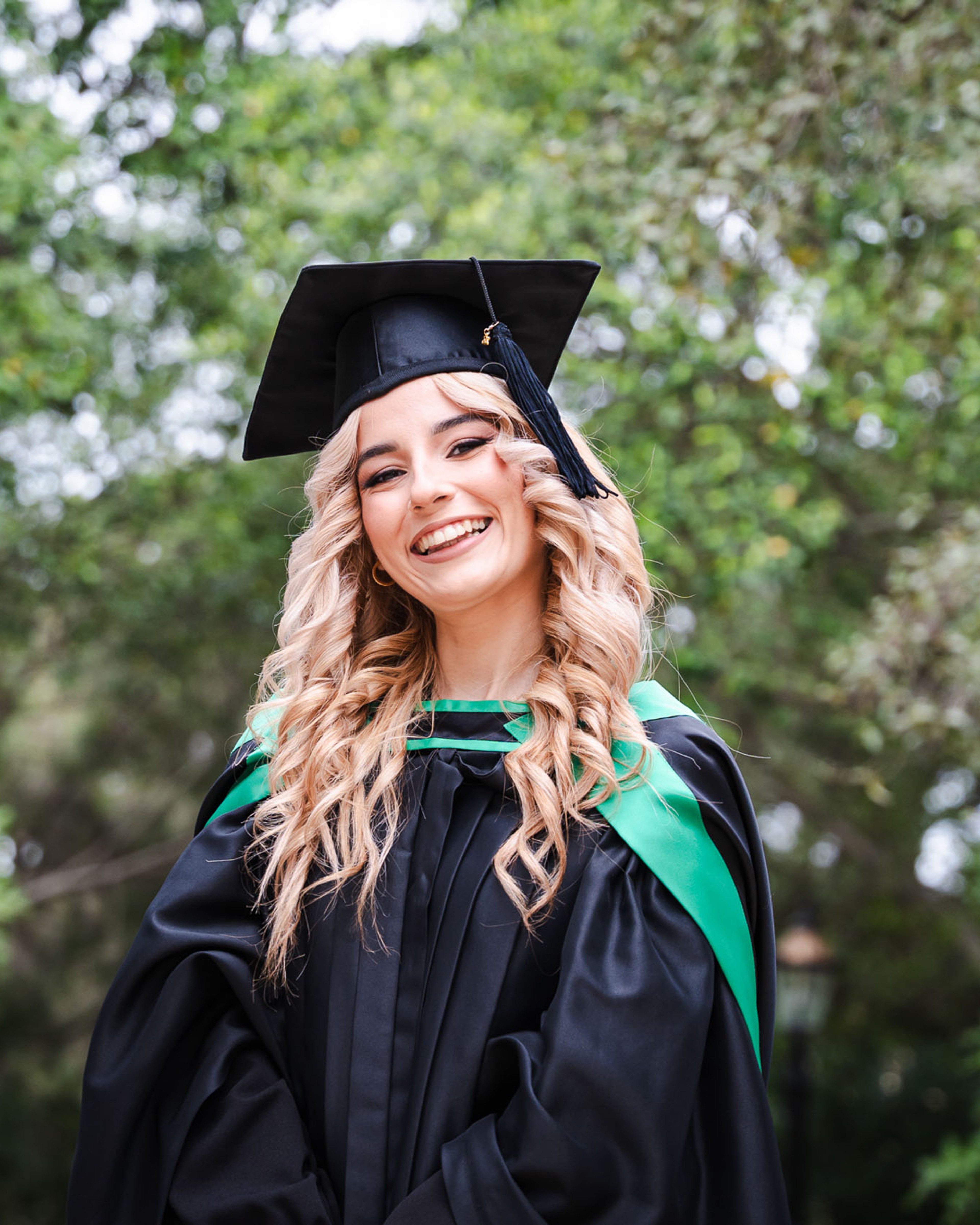 Smiling graduate wearing a cap and green-trimmed gown at Romeo Romano Gardens in Malta.