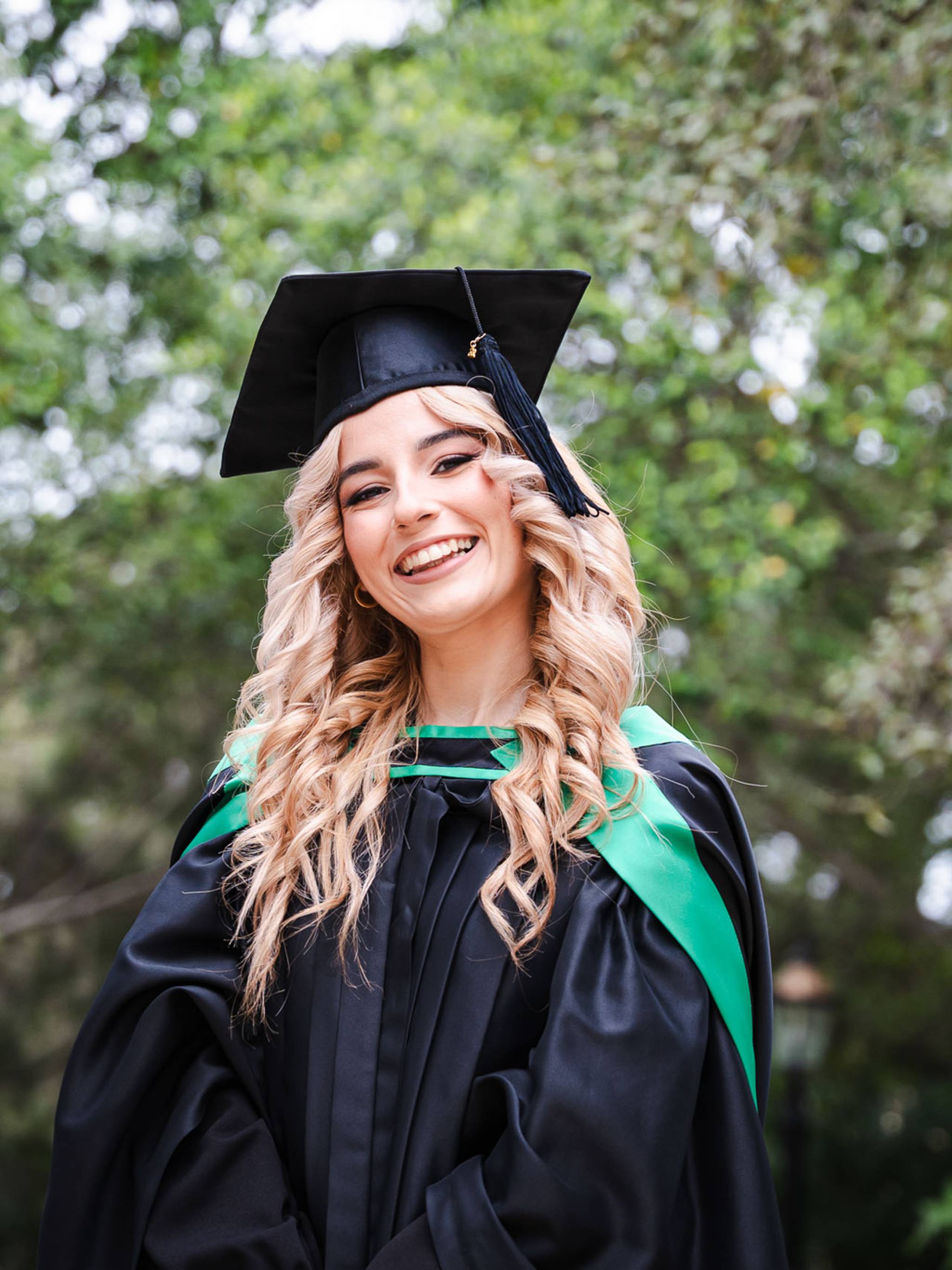 Smiling graduate wearing a cap and green-trimmed gown at Romeo Romano Gardens in Malta.