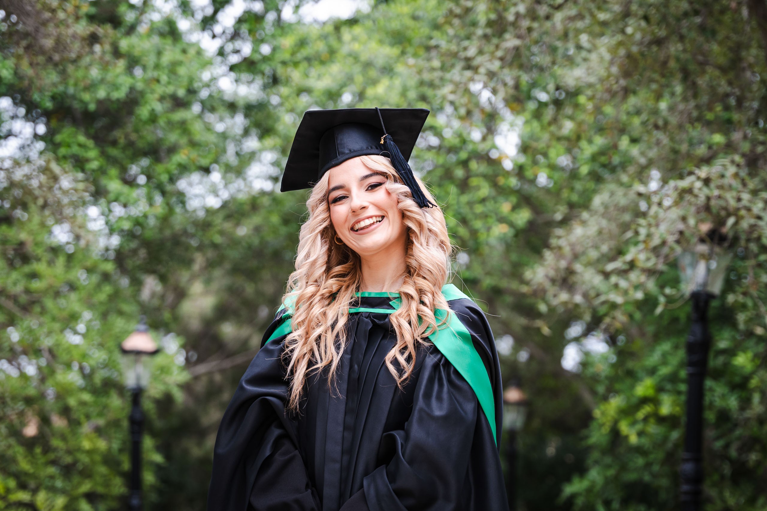 Smiling graduate wearing a cap and green-trimmed gown at Romeo Romano Gardens in Malta.