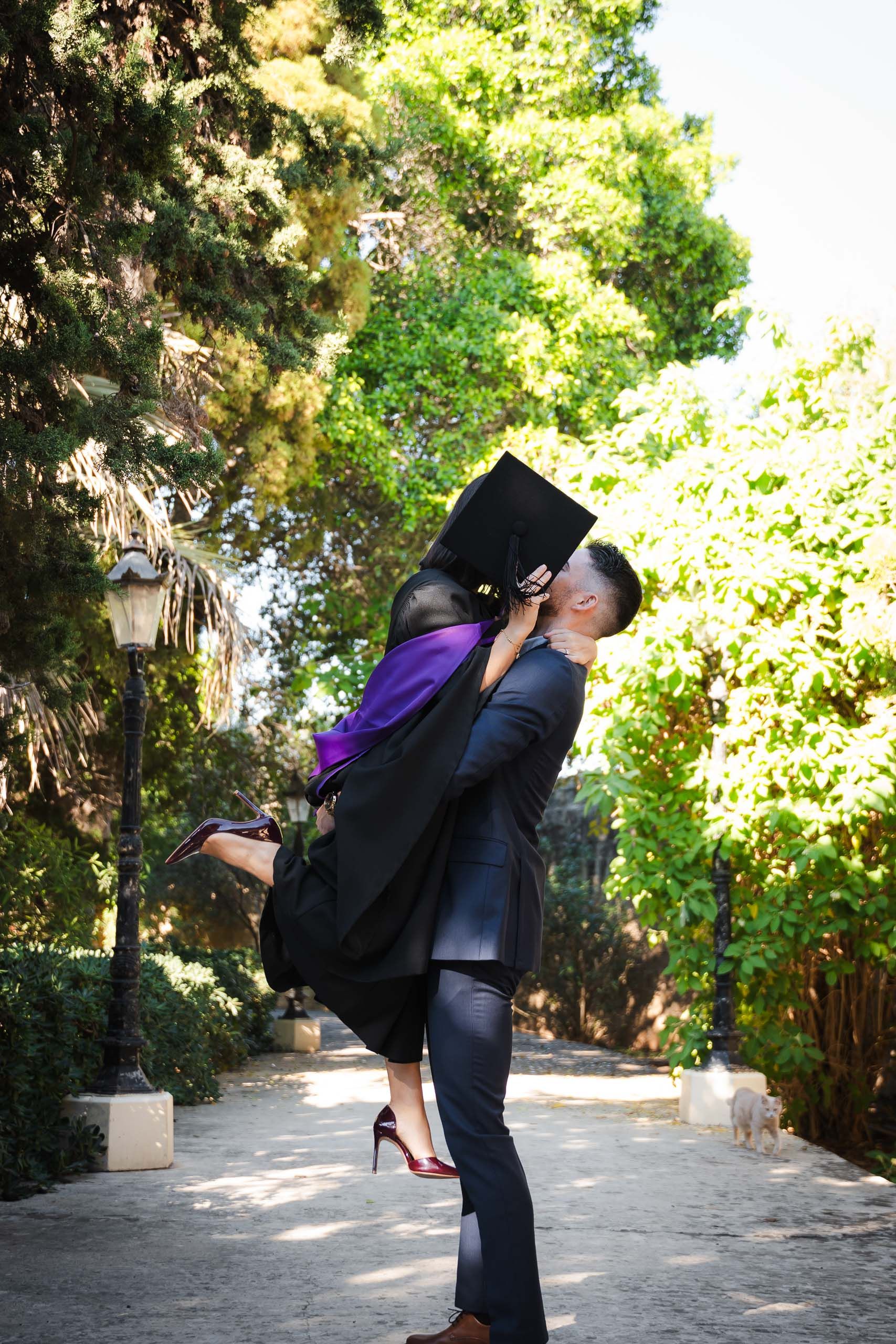 Graduate in a purple-trimmed gown being lifted and kissed by her partner at Romeo Romano Gardens in Malta.  IMAGE 2