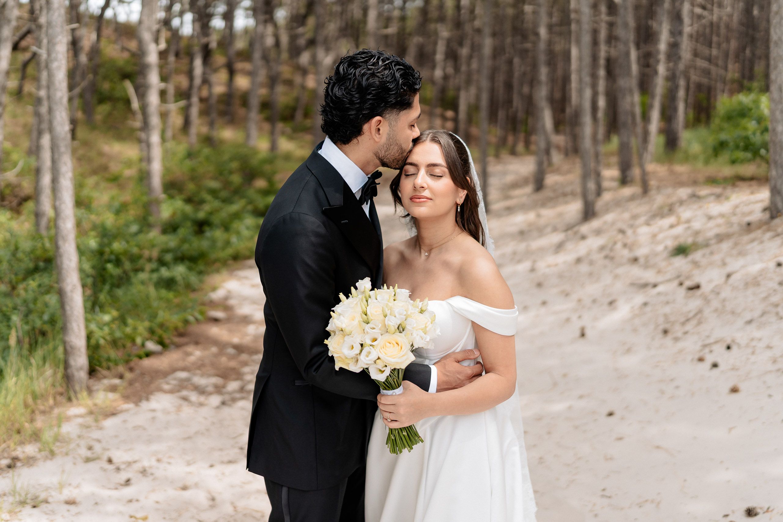 Groom kissing the bride on the forehead during their wedding portrait session at Schoorlse Duinen, Netherlands.