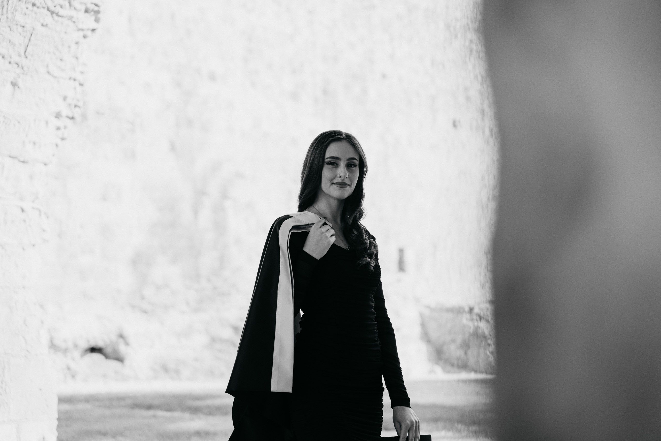 Black-and-white portrait of a female graduate standing in a sunlit limestone passage at Mdina Ditch Gardens in Malta.