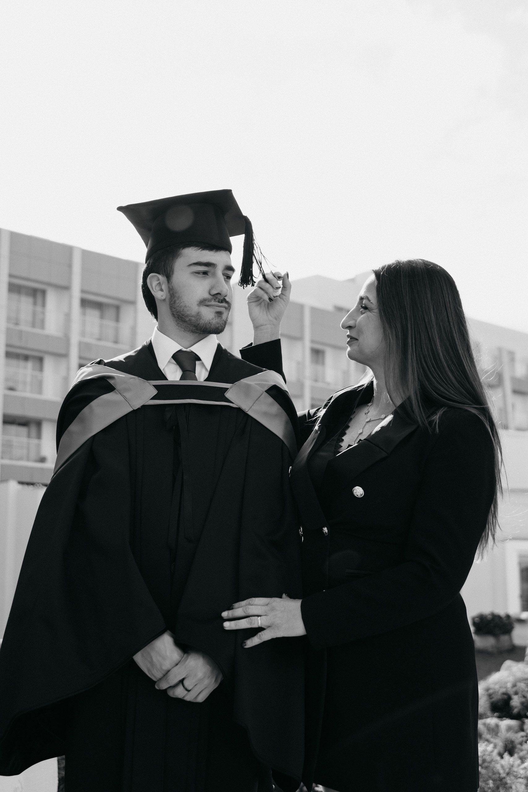 Black-and-white photograph of a mother adjusting her son’s graduation cap at Hilton Malta.