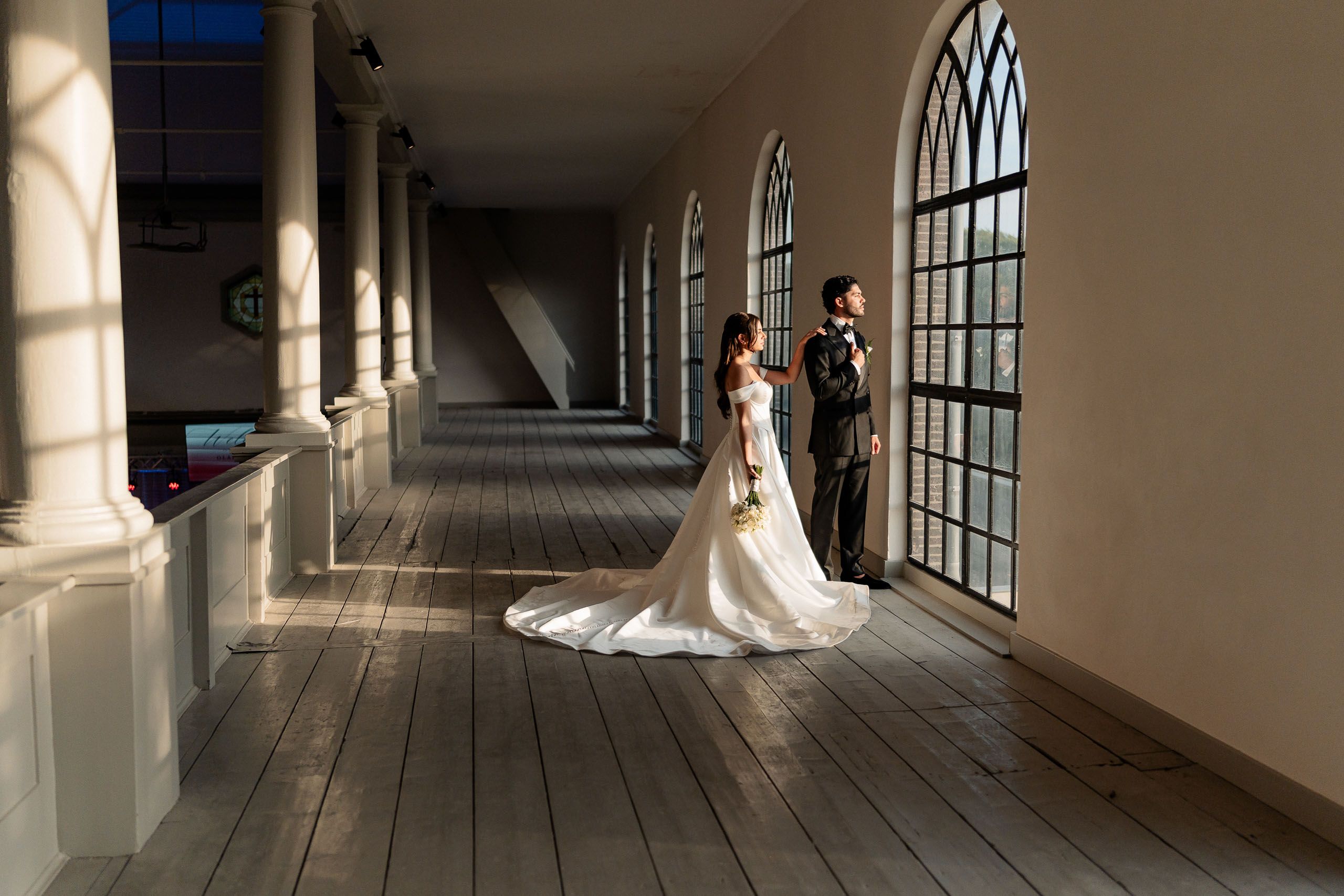 Bride and groom wedding portrait beside tall arched windows inside a church in Den Helder, Netherlands.