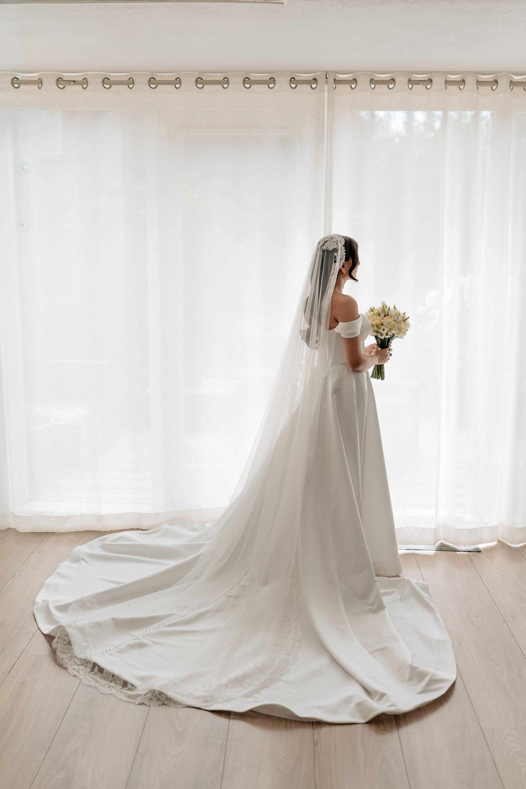 Bride holding her bouquet beside a bright window while getting ready for her wedding in Den Helder, Netherlands.