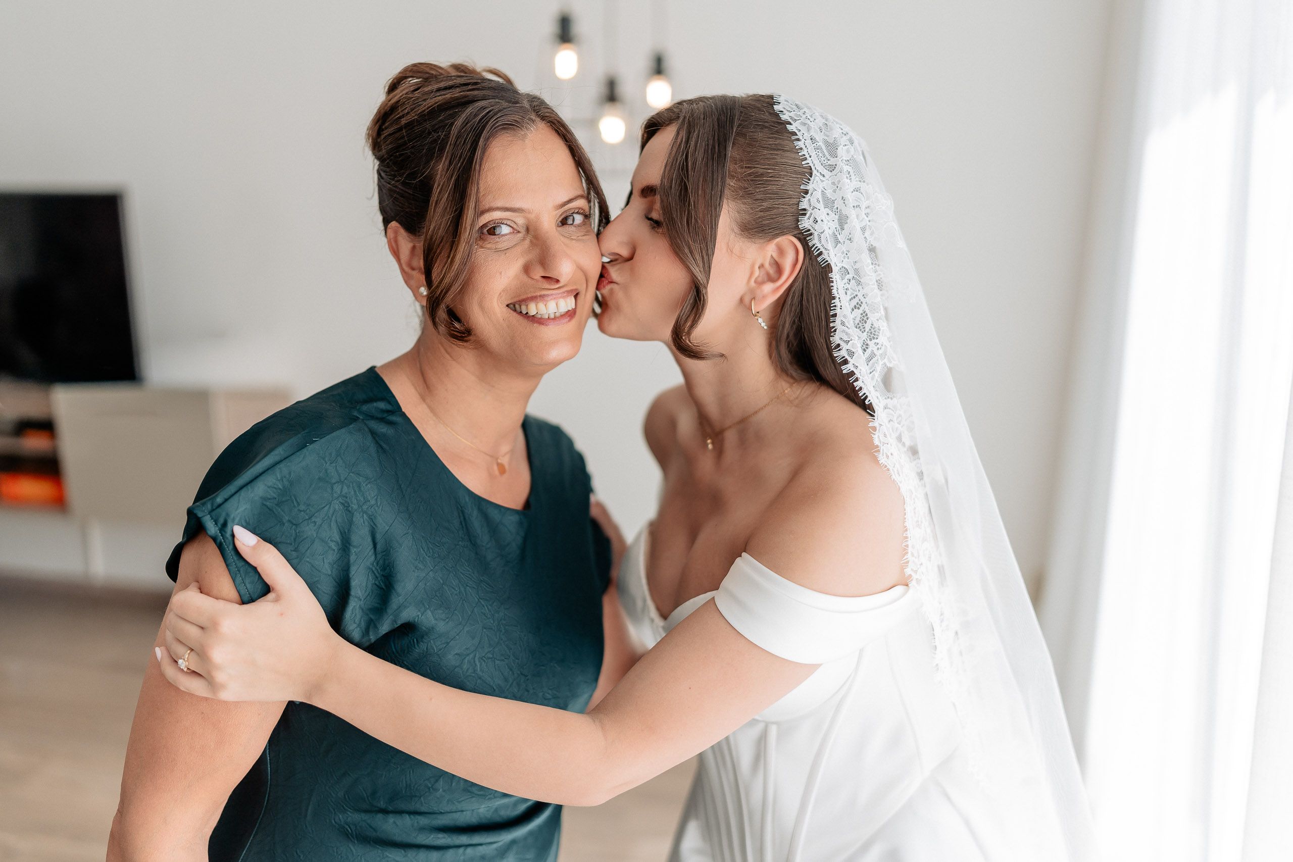 Bride sharing an affectionate moment with a family member while getting ready in Den Helder, Netherlands.