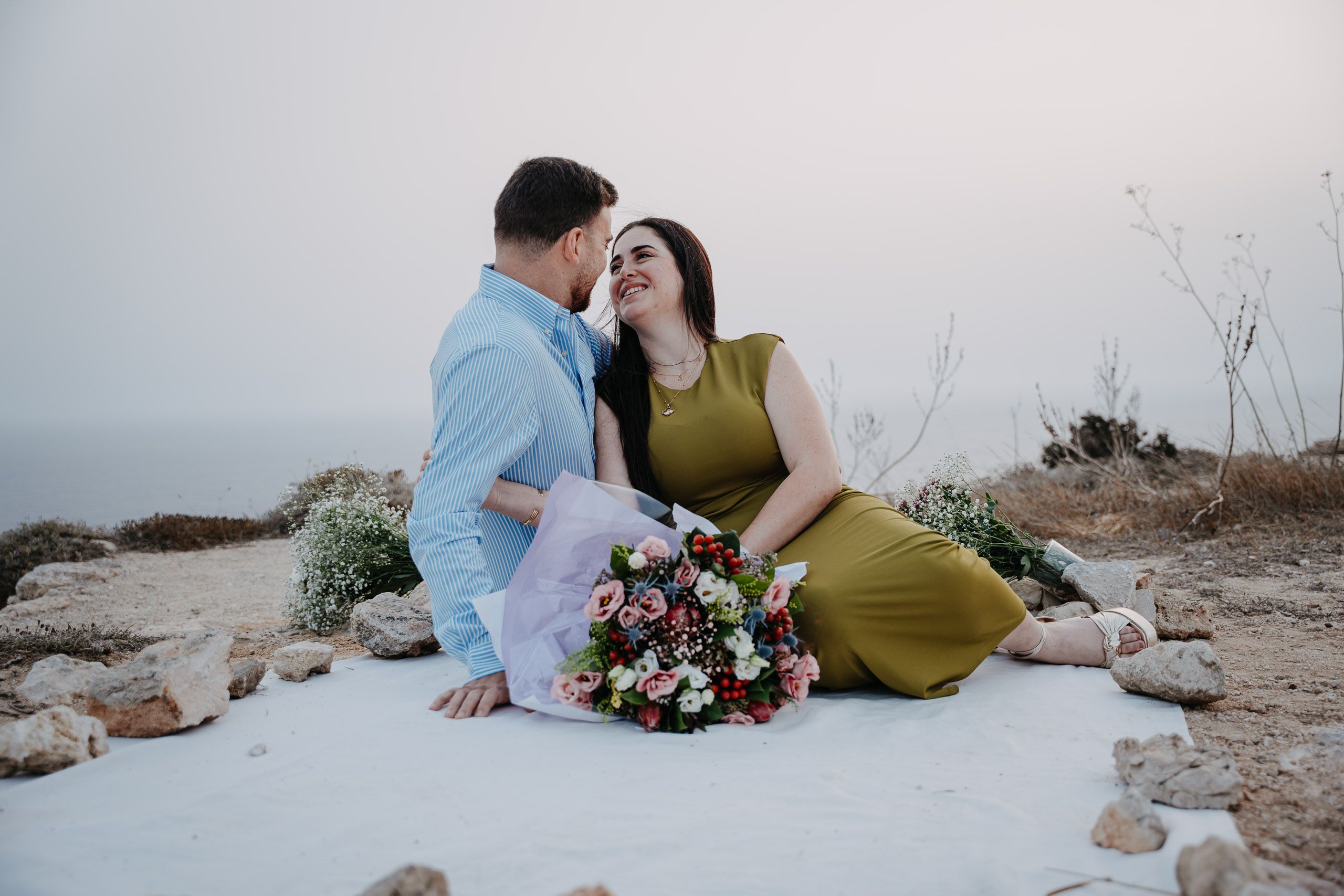 Engaged couple sitting together with flowers during a Dingli Cliffs proposal session in Malta