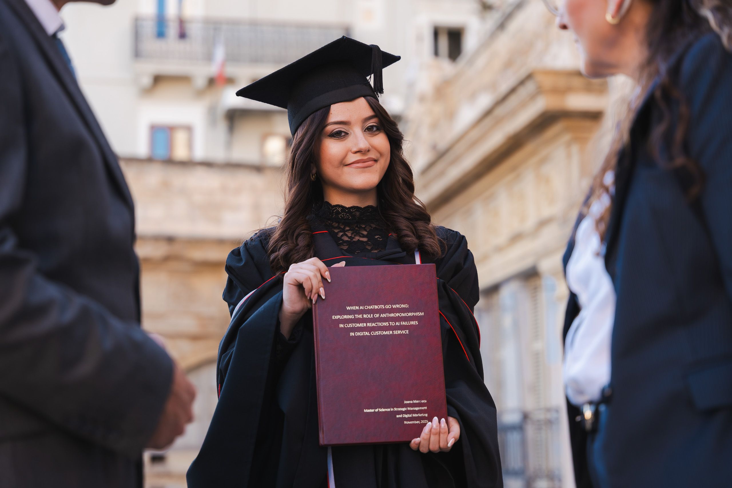 Graduate holding her thesis while surrounded by family during a photoshoot near Victoria Gate, Valletta.