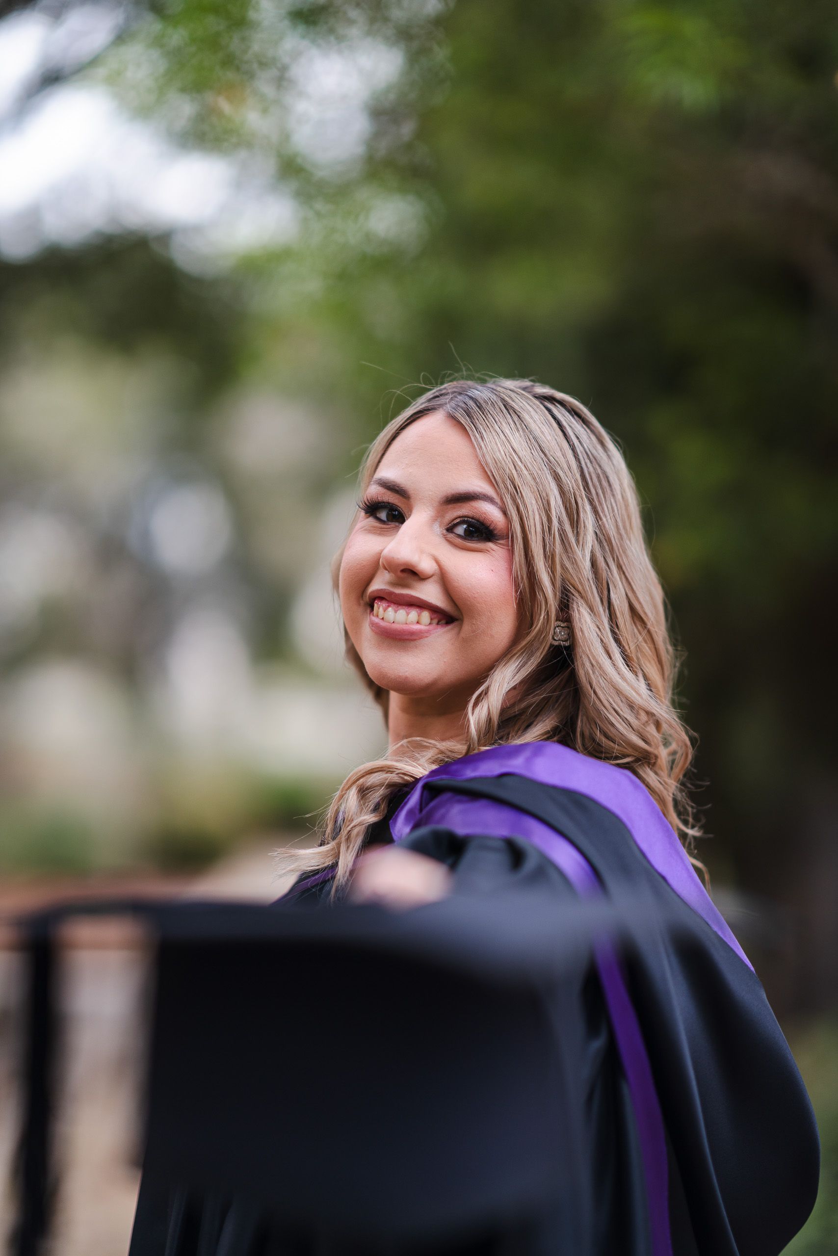 Graduate in a purple-trimmed gown smiling over her shoulder with her graduation cap in the foreground.