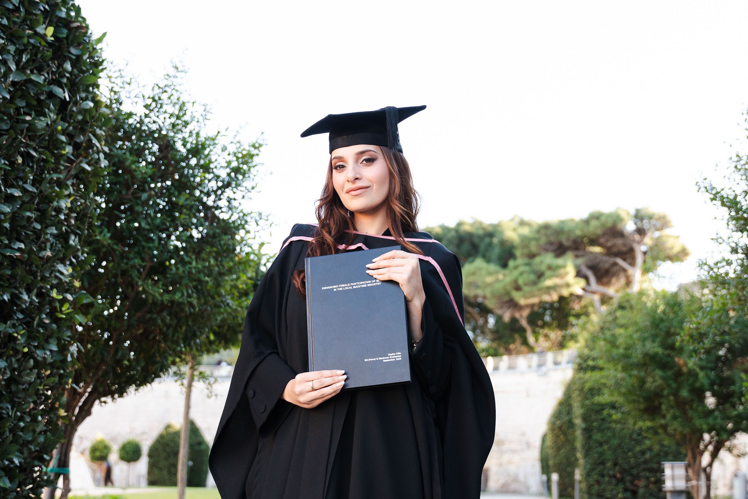 Graduate posing with her dissertation during an outdoor graduation photoshoot in Mdina, Malta.