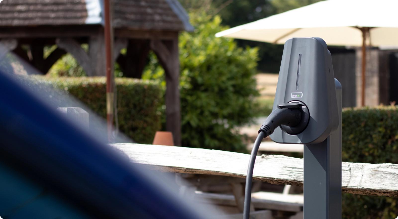 A Brim charger on a post beside a wooden fence, cable plugged in