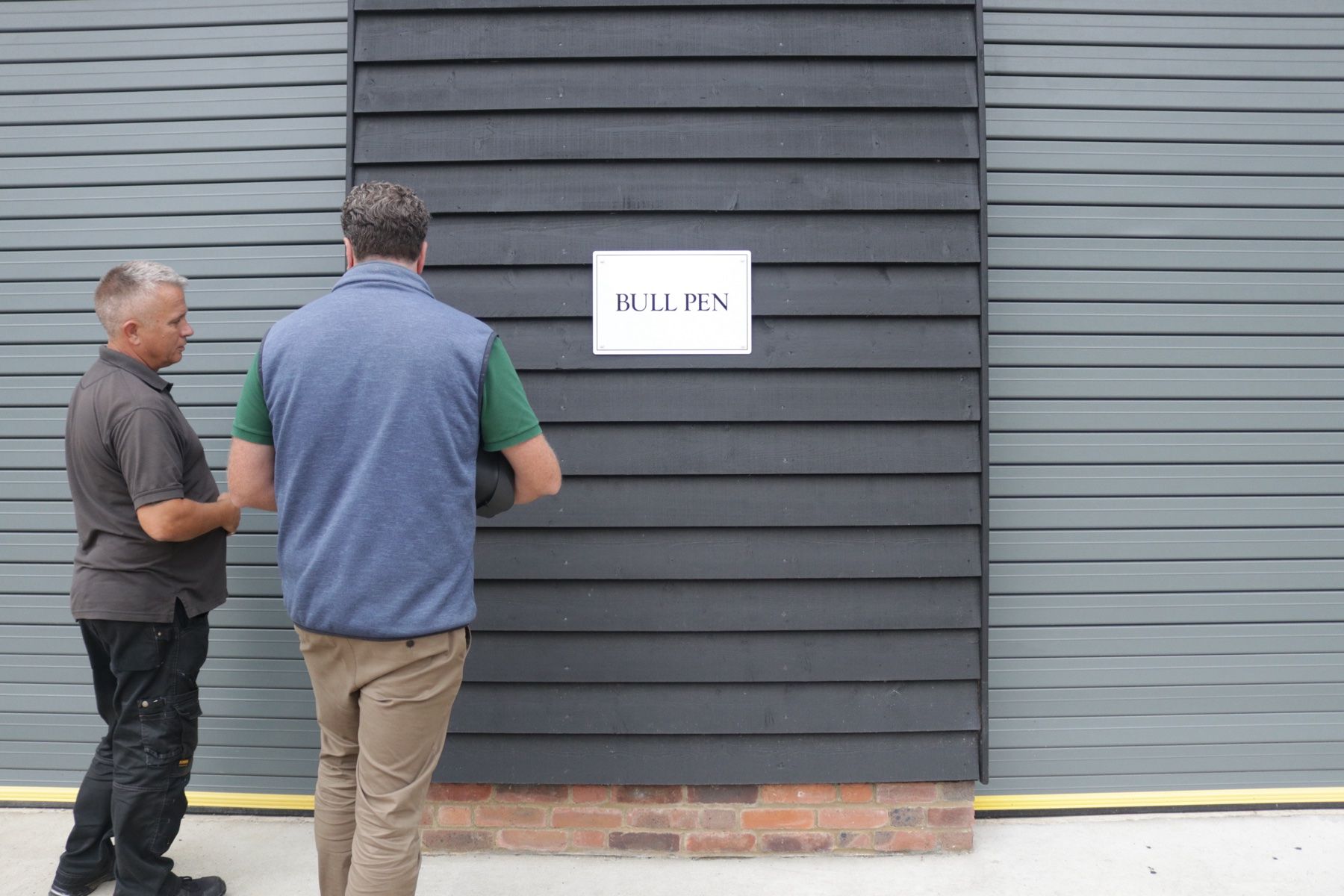 Two people at a wall-mounted charger on a clad workplace building