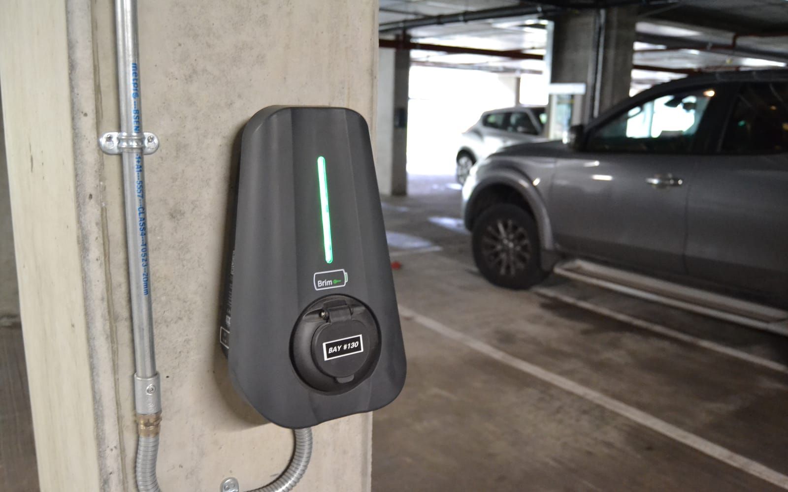 A Brim charger on a concrete column in an undercroft residents' car park, cars in the bays beyond