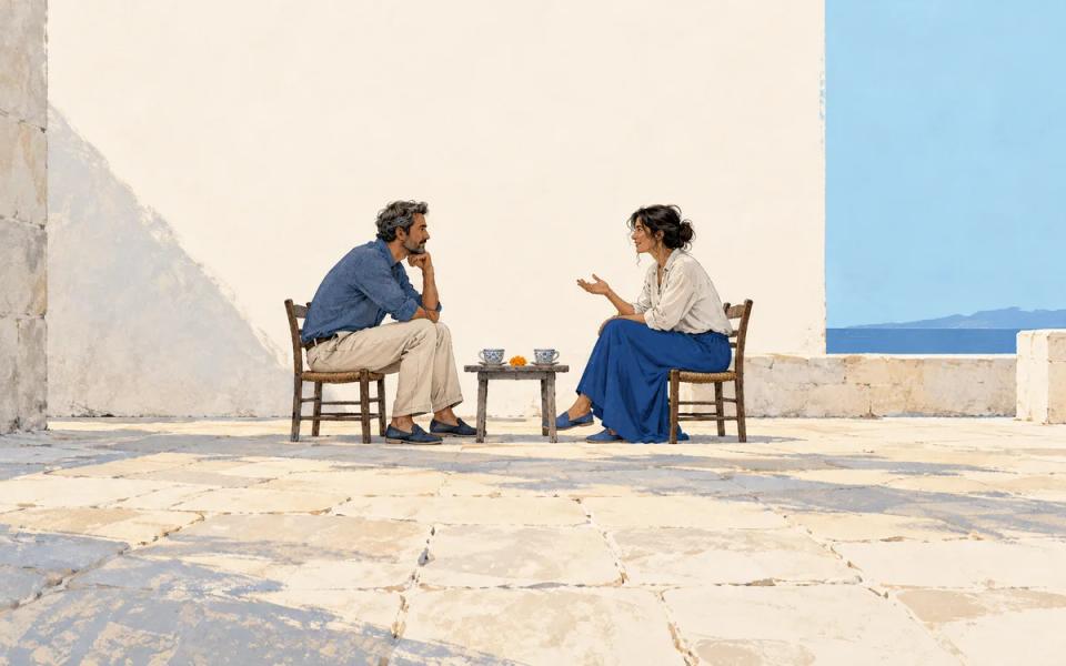 Two people seated facing one another with a small table and cups between them.