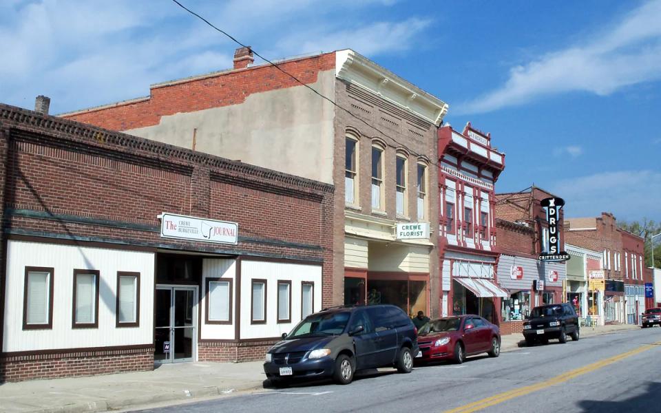 Downtown Crewe street with brick storefronts, parked cars and a blue sky.