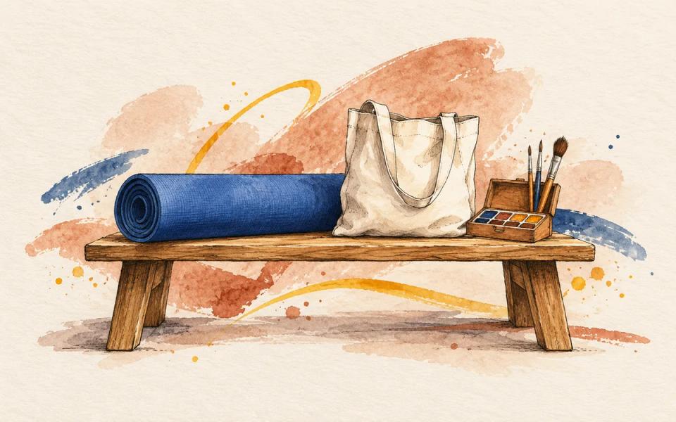 A rolled blue yoga mat, canvas tote and paintbrushes resting on a wooden bench.