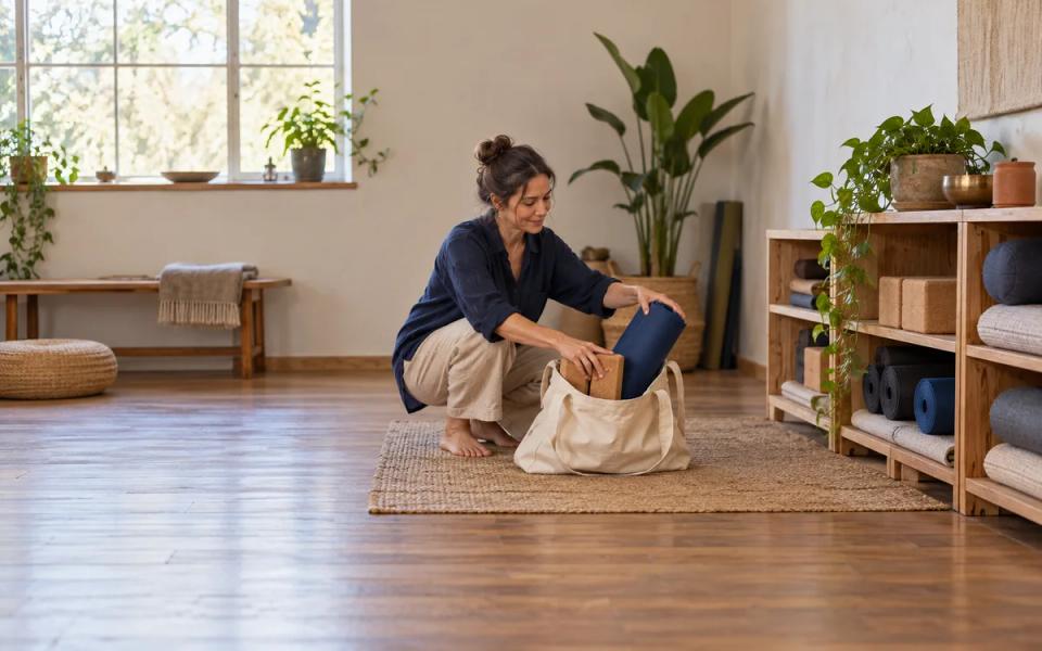 A woman placing a rolled blue mat and practice equipment into a cotton carry bag.