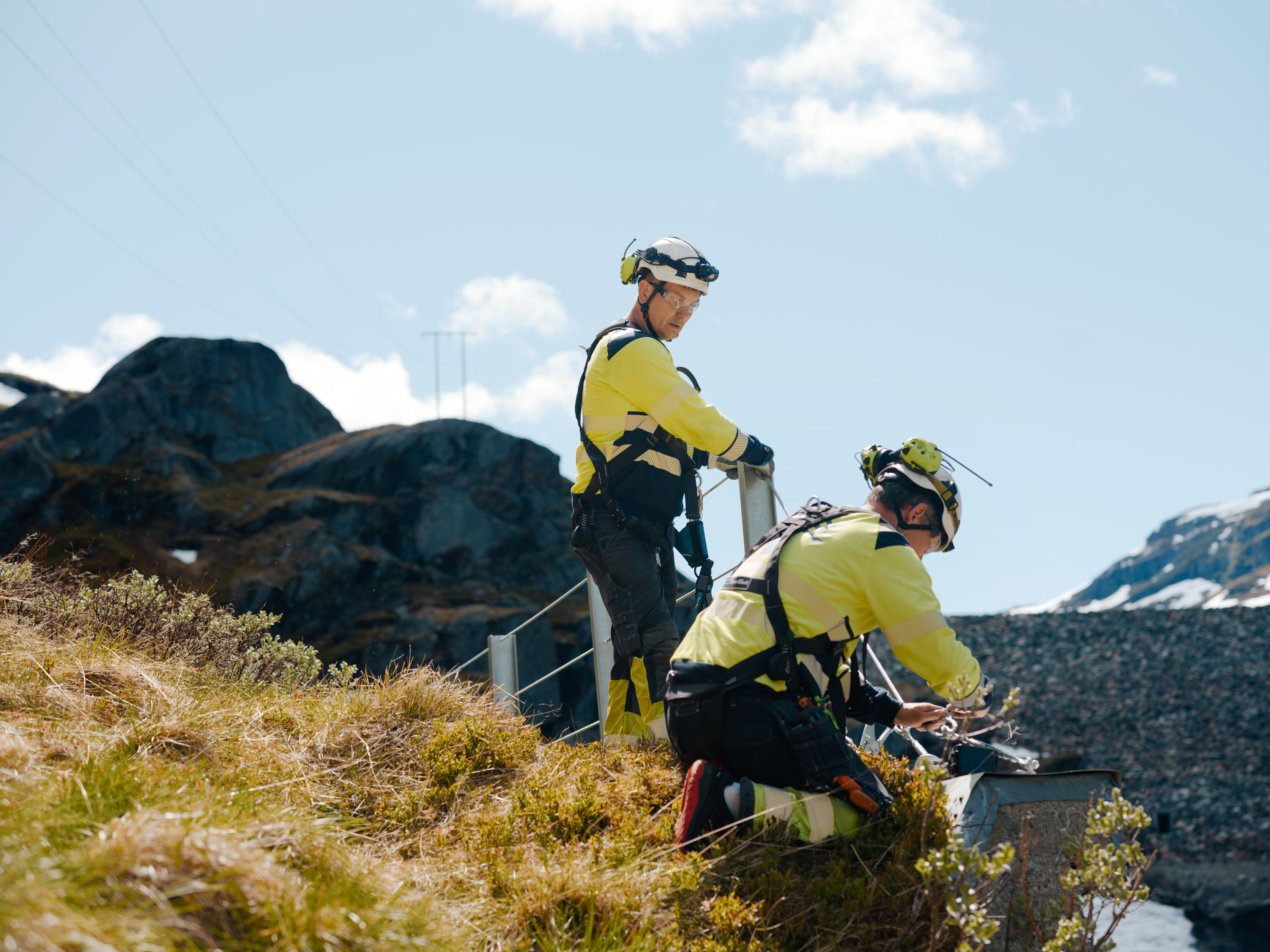 To menn i vernetøy som jobber ved dam på fjellet. 