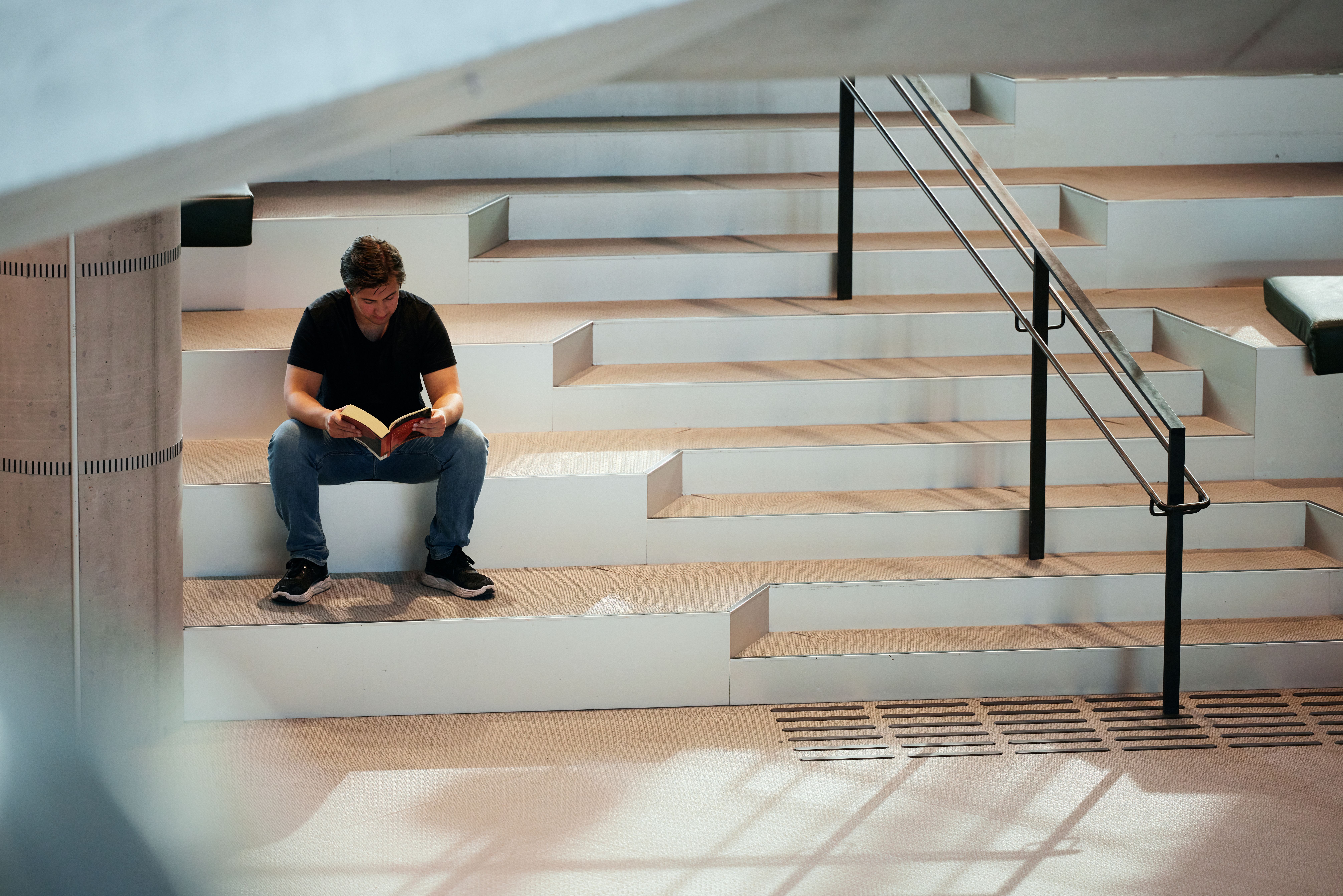 Mann sitter i trapp på Deichman Bjørvika og leser en bok.