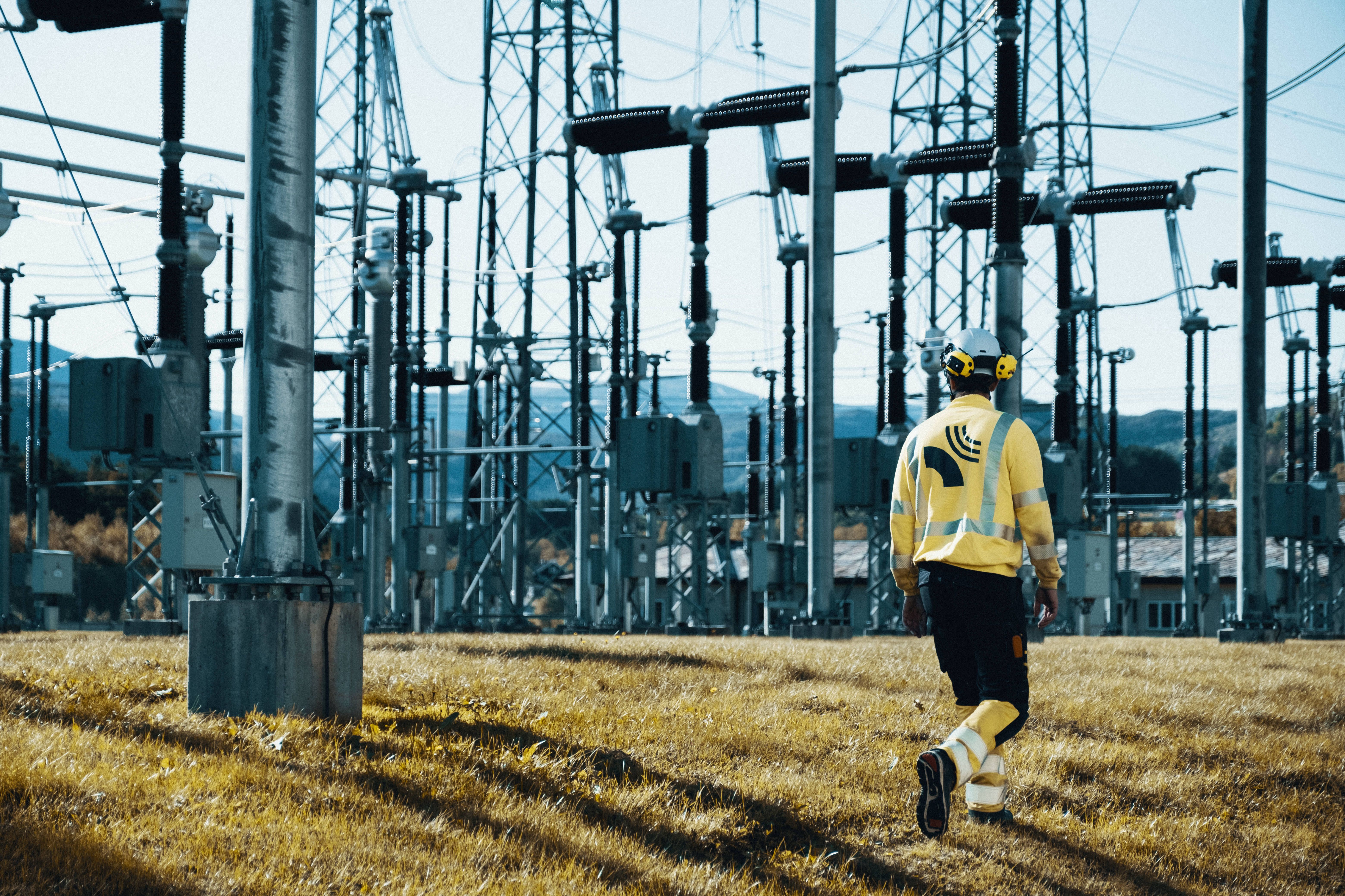 En mann i vernetøy går foran en strømstasjon. 