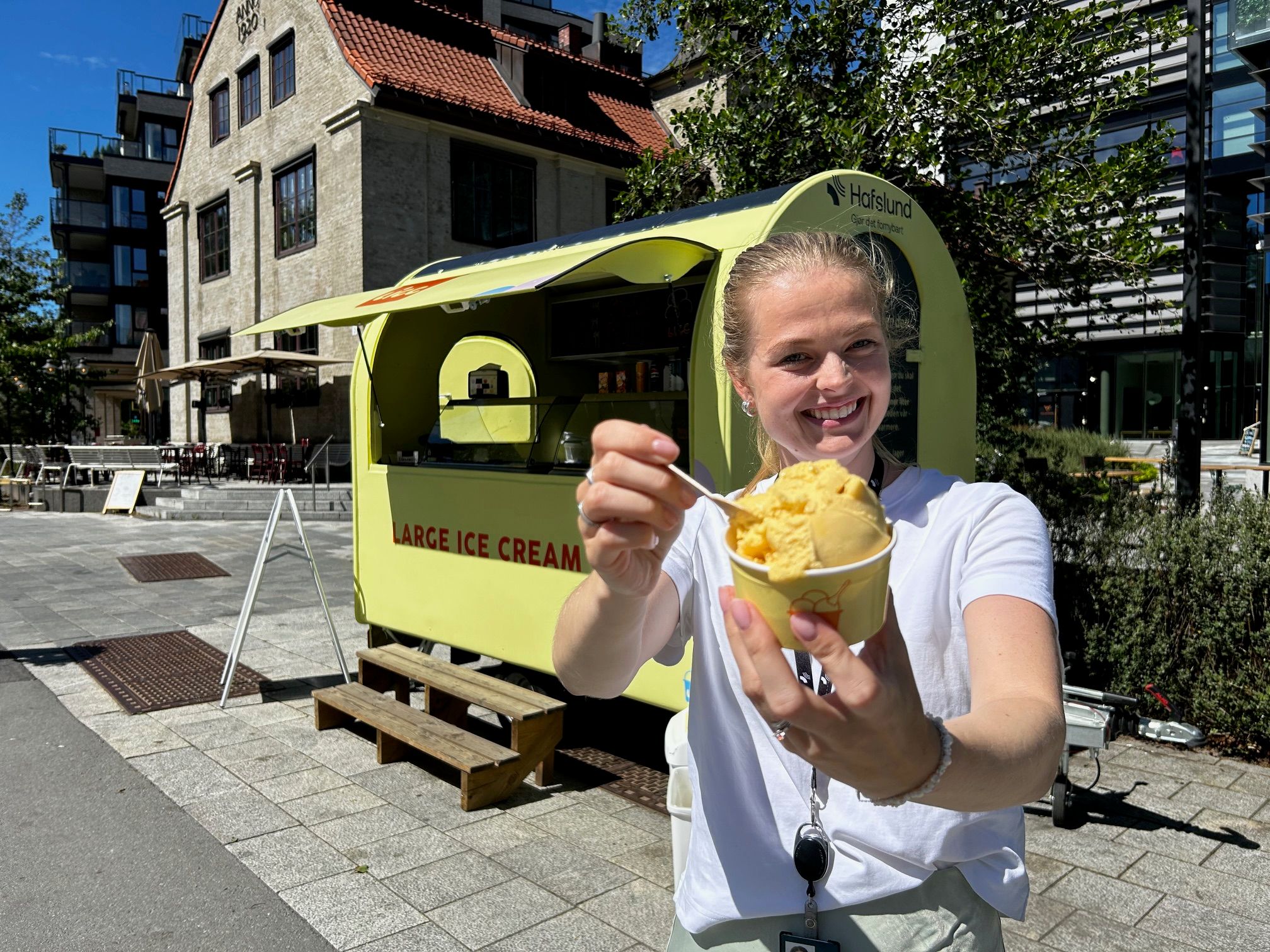 Smilende kvinne holder et beger med iskrem, iskremvogn i bakgrunnen