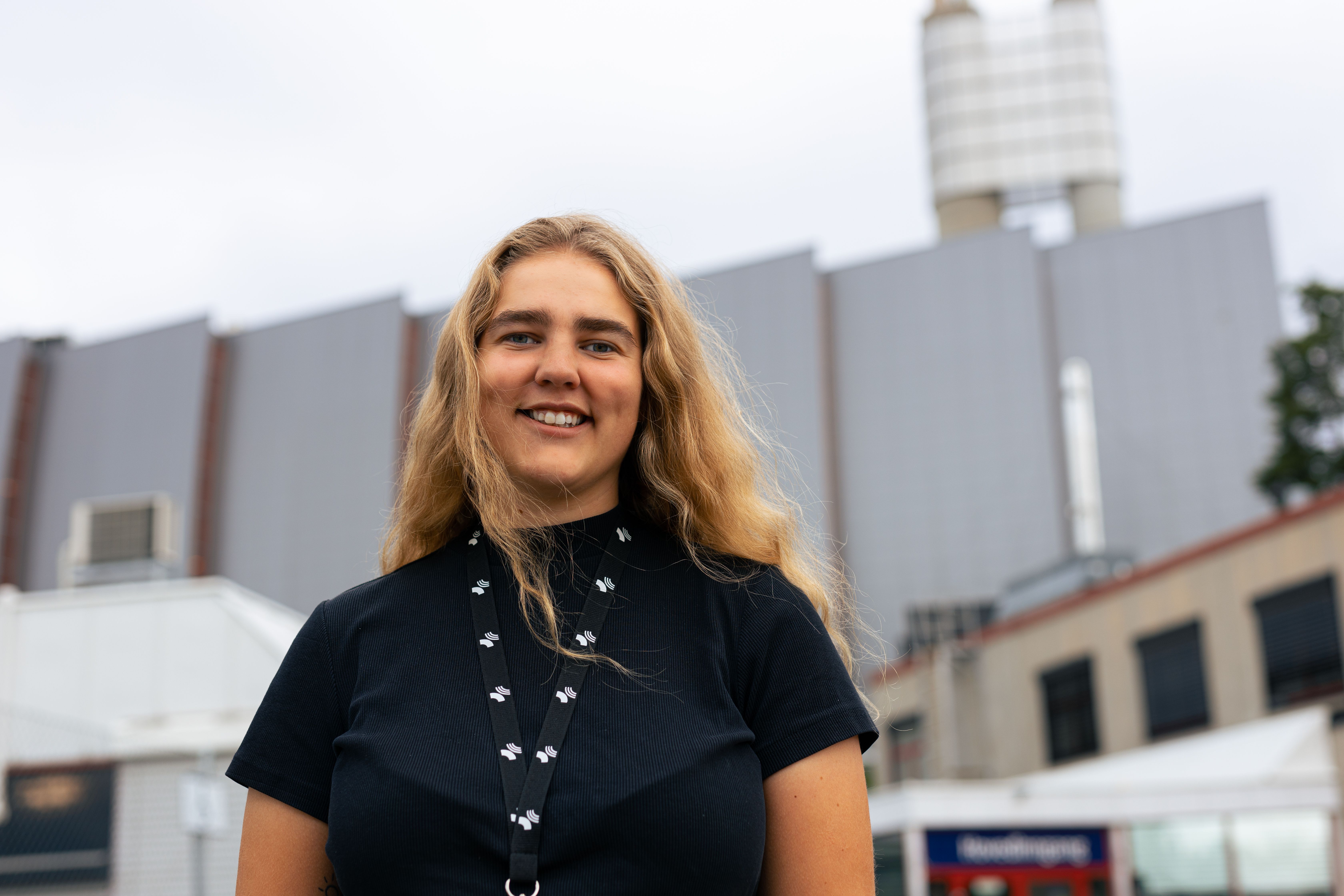 Smilende kvinne utenfor en stor bygning med piper