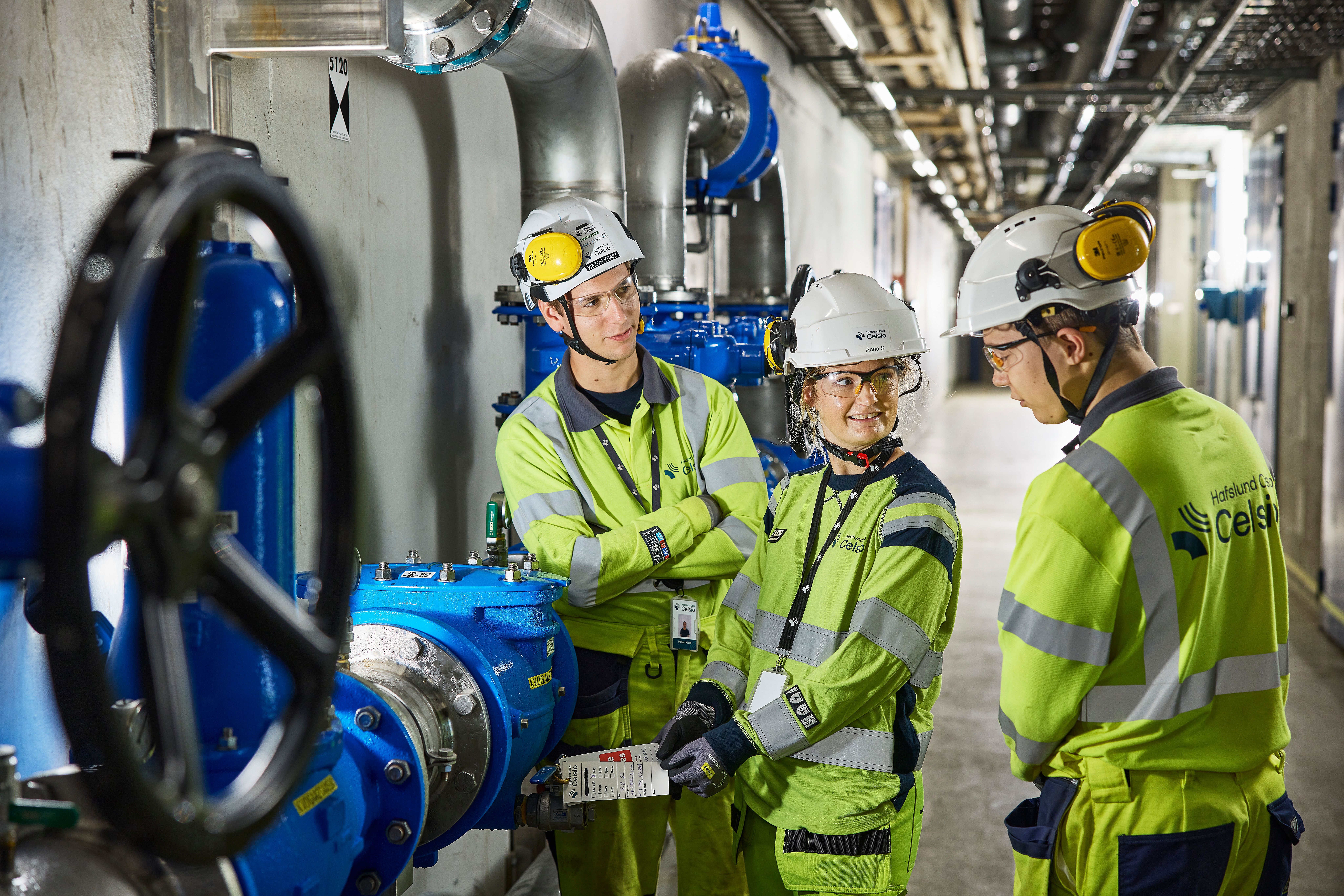 Tre mennesker i vernetøy inni en varmesentral